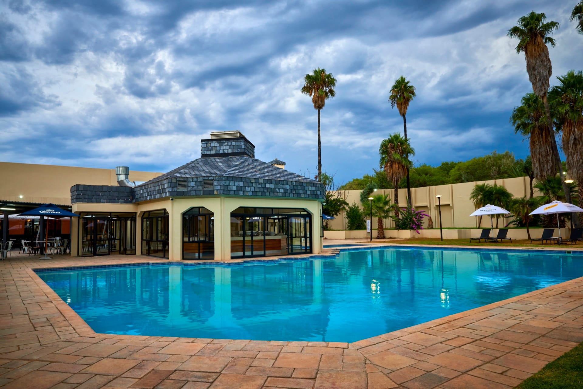 Turquoise pool and pavilion framed by palms at dusk at Mmabatho Palms, Mahikeng